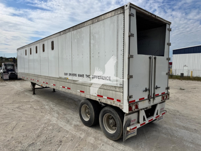 Trailer side and rear showing metal chip trailer with windows along the side and rear ramp open. Dual rear wheels, stock markings and safety decals visible.