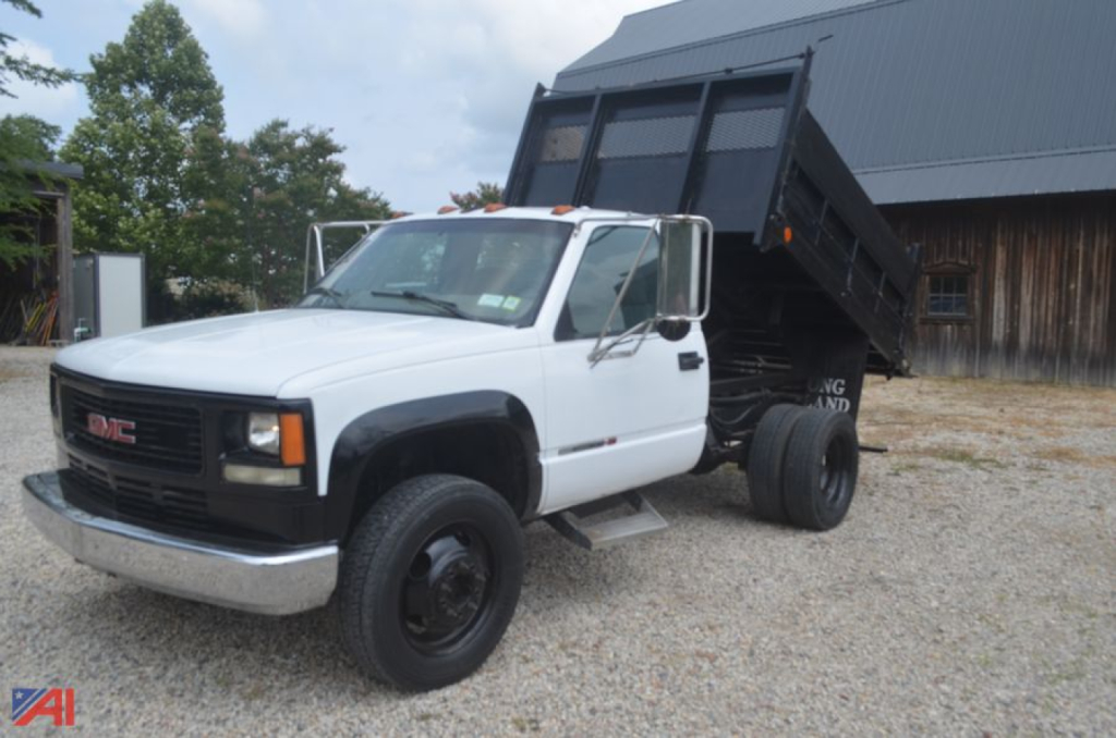 GMC Sierra 3500 dump truck in white cab with black dump bed, front view, two-tone color, parking lot gravel surface.