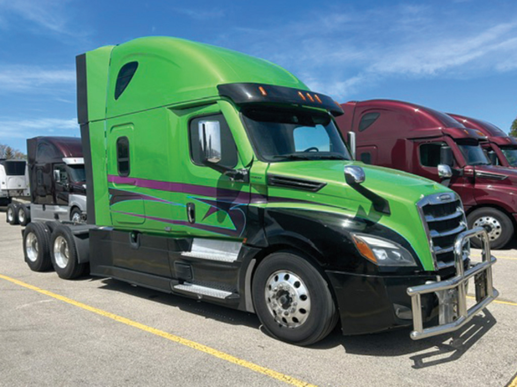 Green Freightliner Cascadia126 sleeper cab truck with purple and black graphics, front bull bar, parked among other trucks.