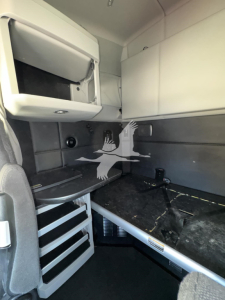 Kenworth T680 sleeper cab interior showing storage compartments, desk area, and ladder with steps.