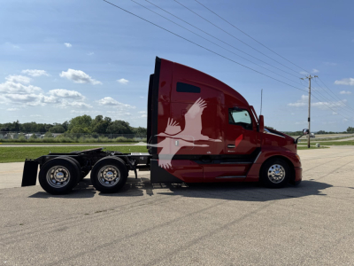 Kenworth T680 in-service truck with red sleeper cab, side view showing chassis and wheels, no visible text on body.