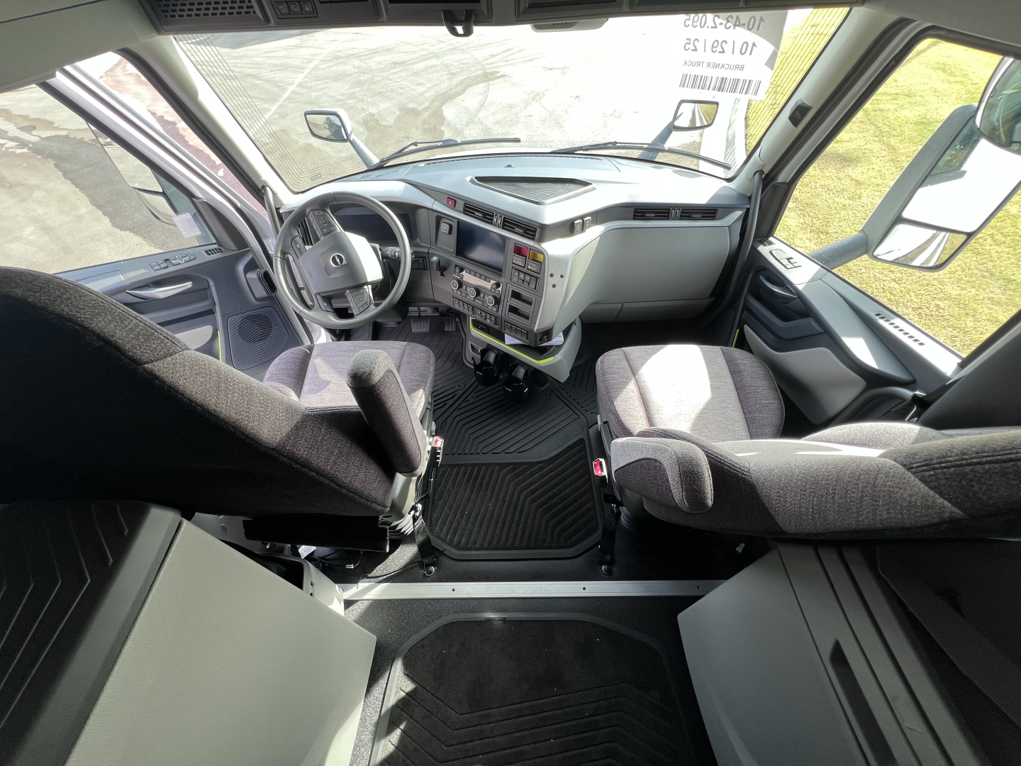 Truck cab interior of a Volvo VNL64T840 showing driver's seat, steering wheel, dashboard, and passenger seat with center console. Visible floor mats and door panels.