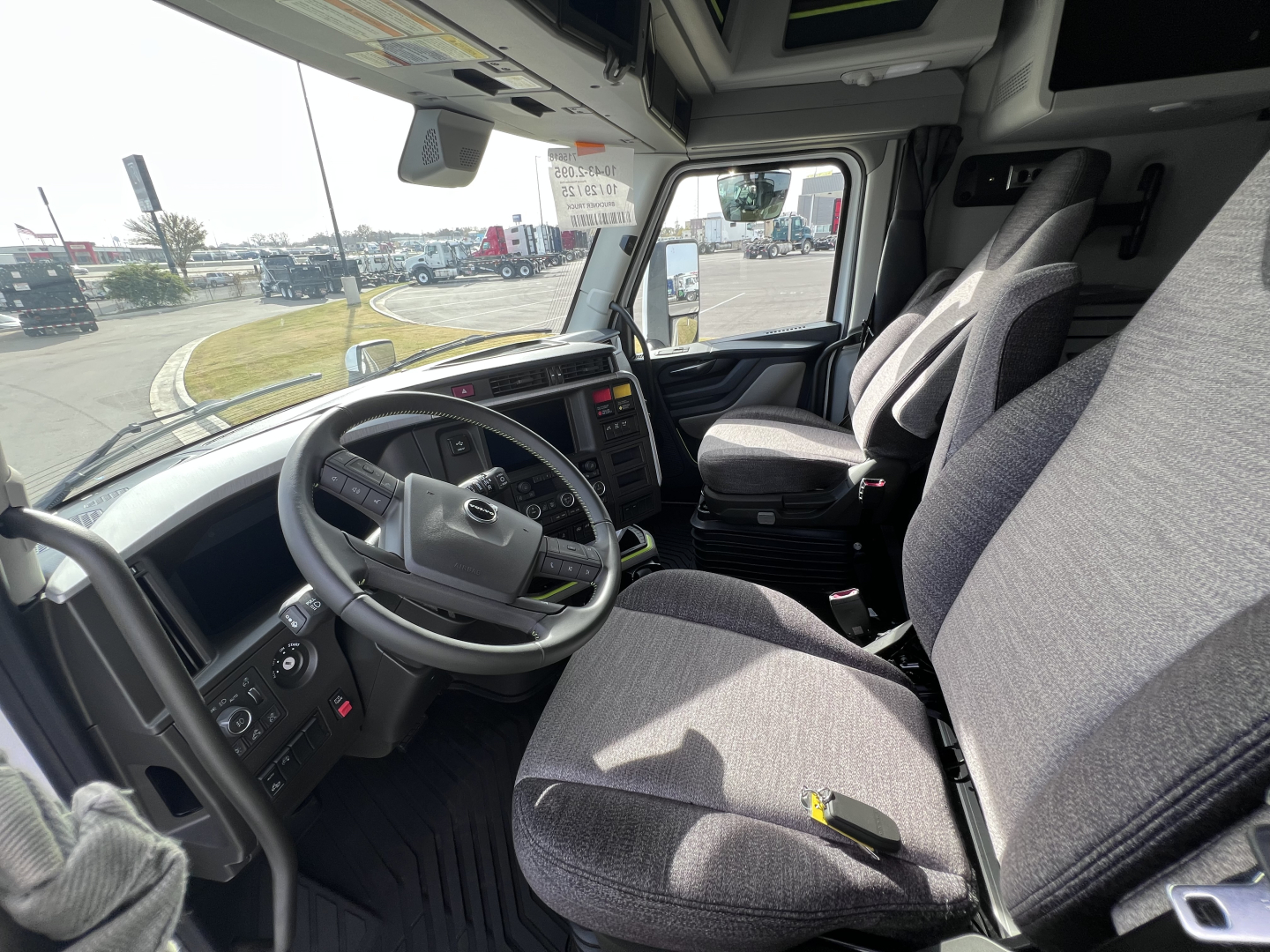 Volvo VNL64T840 truck cabin interior showing steering wheel, dashboard, and driver and passenger seats with grey fabric upholstery.