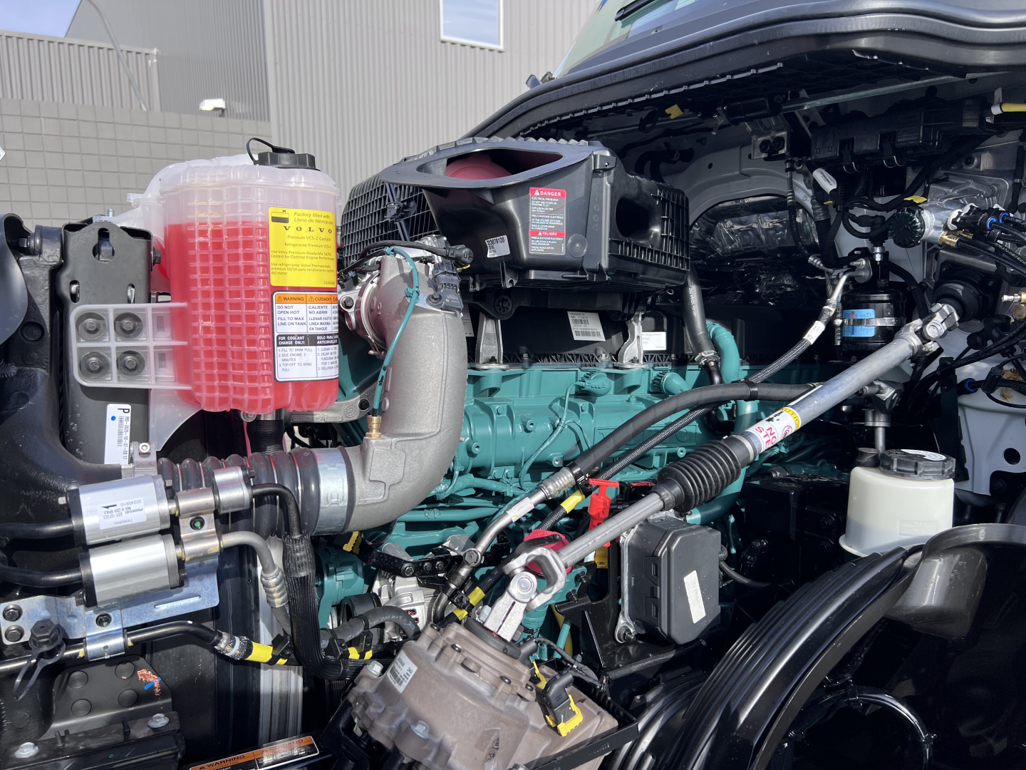 Volvo VNL64T840 engine bay with coolant reservoir, turbo, hoses, and electrical connectors visible.