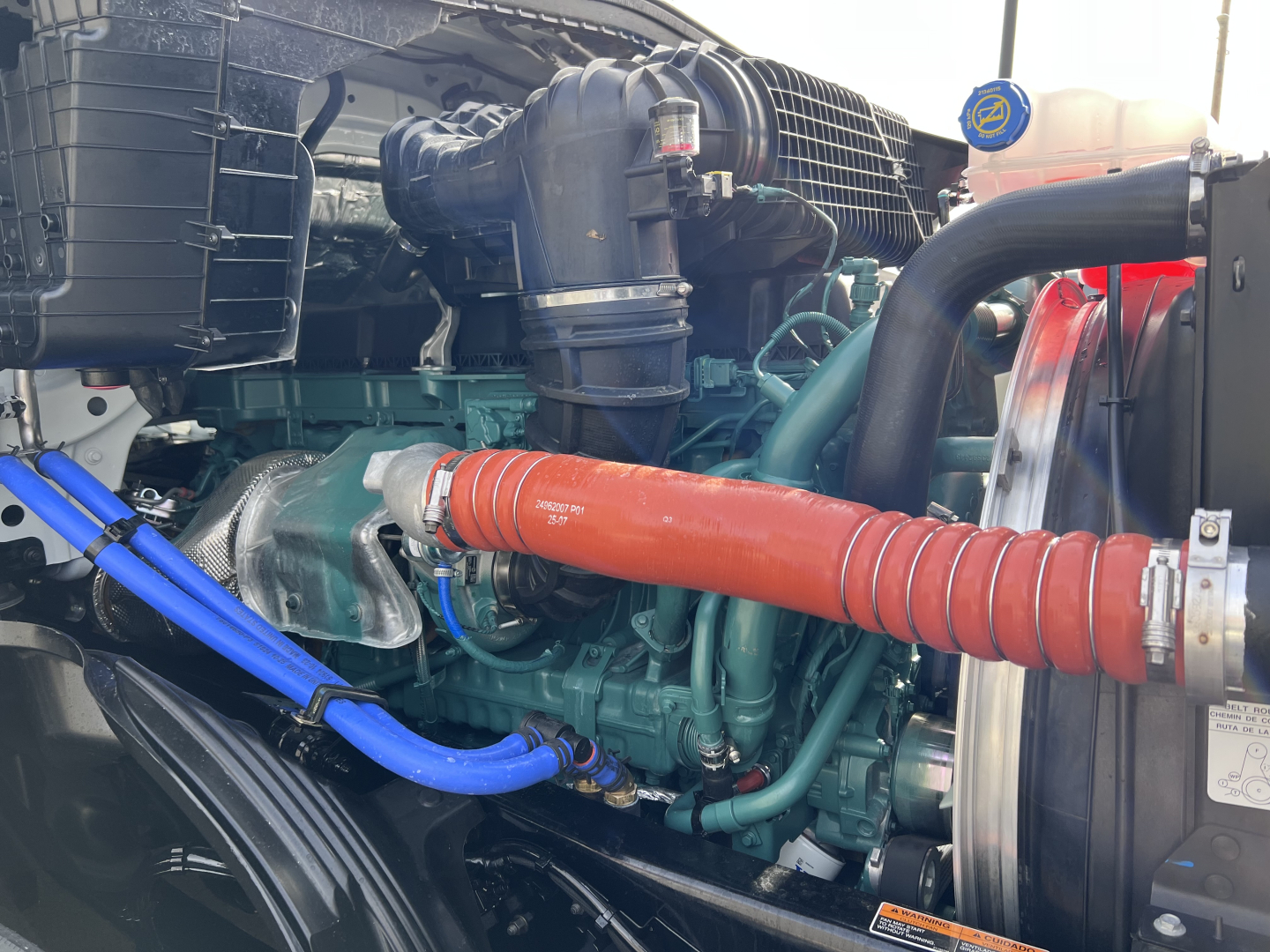 Volvo engine bay showing a green engine with orange turbo hose, blue hoses, and a large black intercooler piping; visible components include radiator and belts.