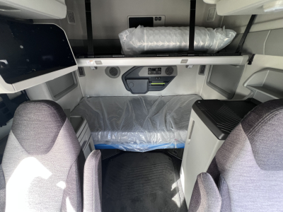 Cab interior of a Volvo VNL truck sleeper berth with control panel and storage area; plastic-covered bed platform visible and seating area in foreground.