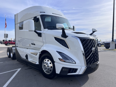 New white Volvo VNL64T840 truck in a dealership lot. Front grille, cab-over design, large mirrors, and side windows.