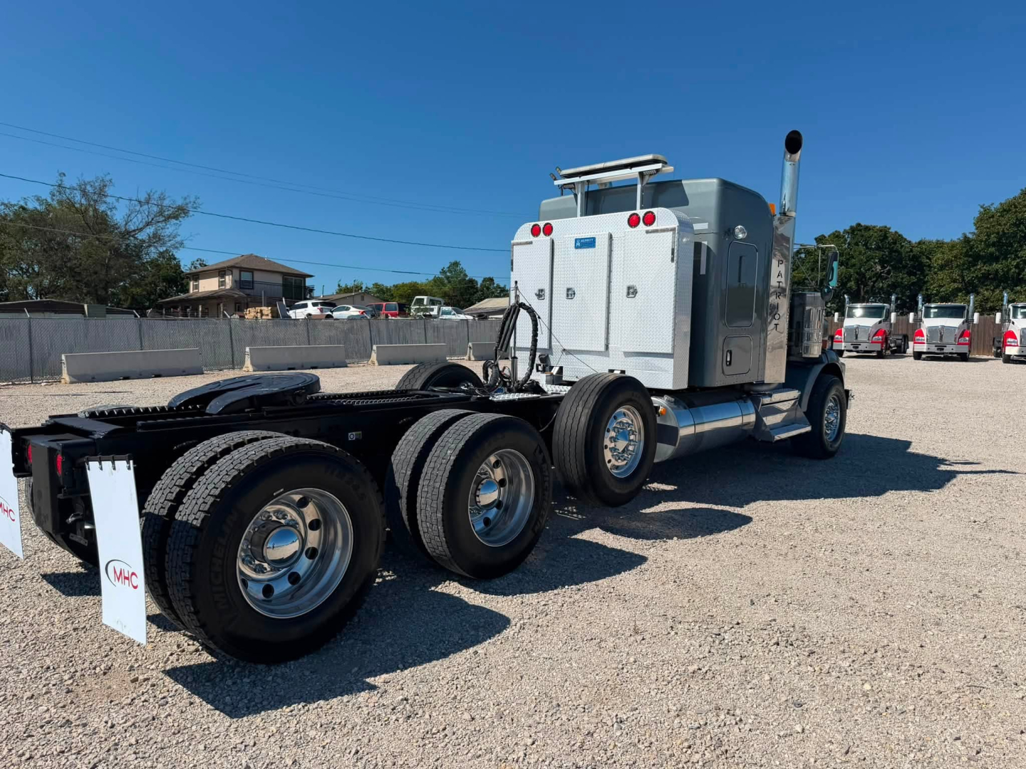 Kenworth T800W truck chassis and cab rear view showing dual rear axles and fifth wheel, with various fuel tanks and exhaust stack.