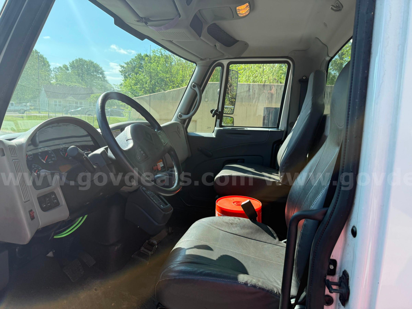 Cab interior of a 2009 International 4400 tow truck showing steering wheel, dashboard, two front seats, and a red bucket on the passenger seat.