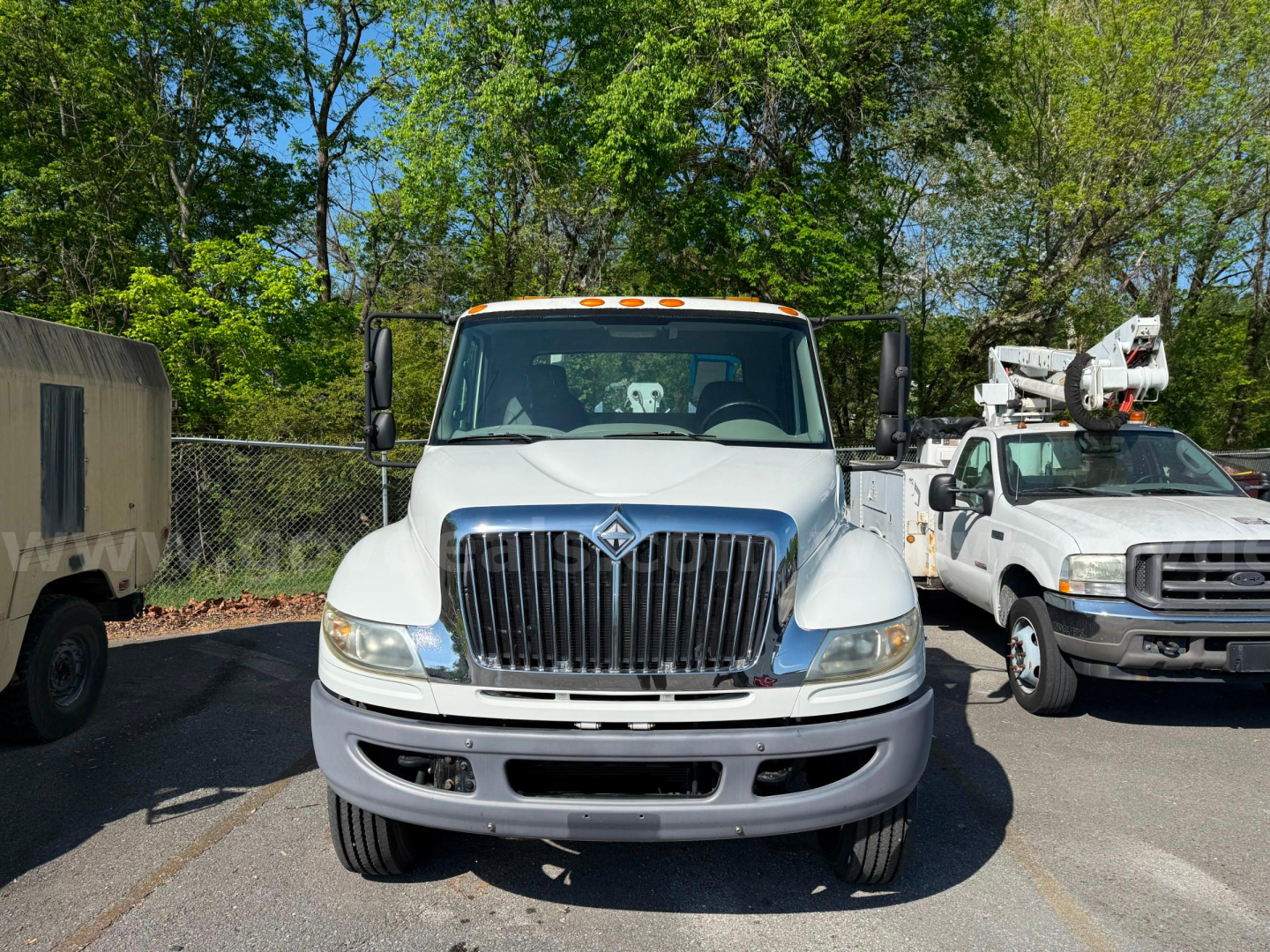 Front view of a white 2009 International 4400 tow truck with chrome grille and large bumper, parked outdoors near other trucks.