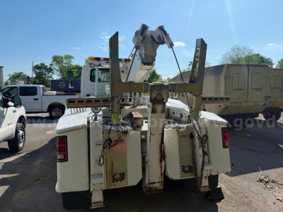 Tow truck rear view with large hydraulic lift arms and white storage compartments on each side. Visible labels and control lines, some rust-free metal, blue sky.