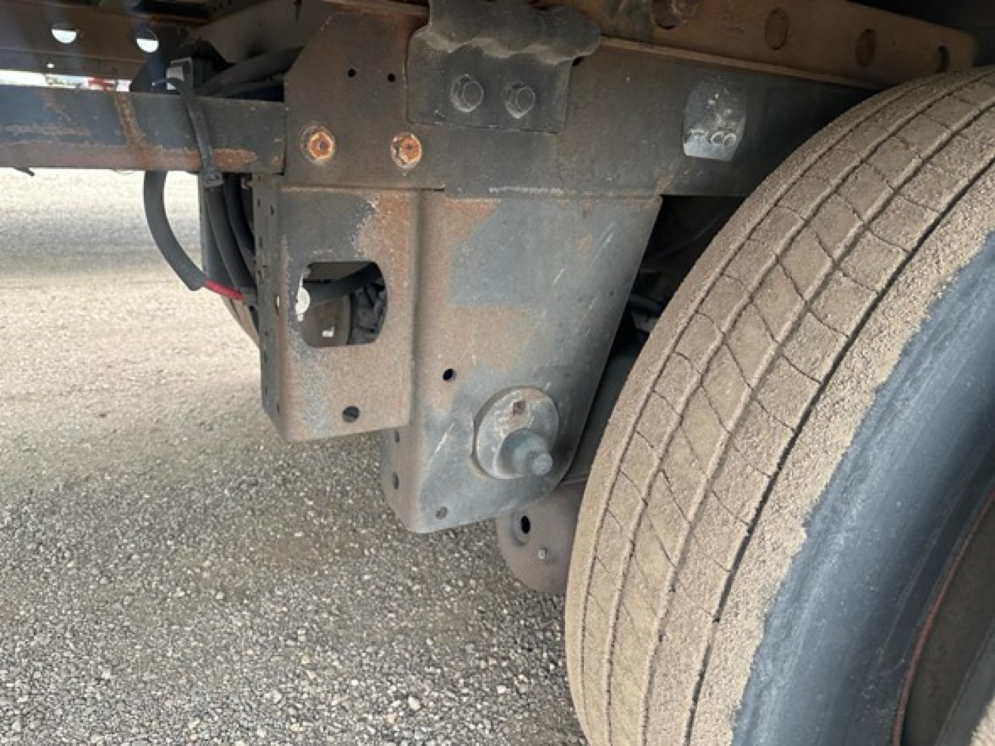Trailer undercarriage showing metal frame with bolts and a dual rear wheel in view.