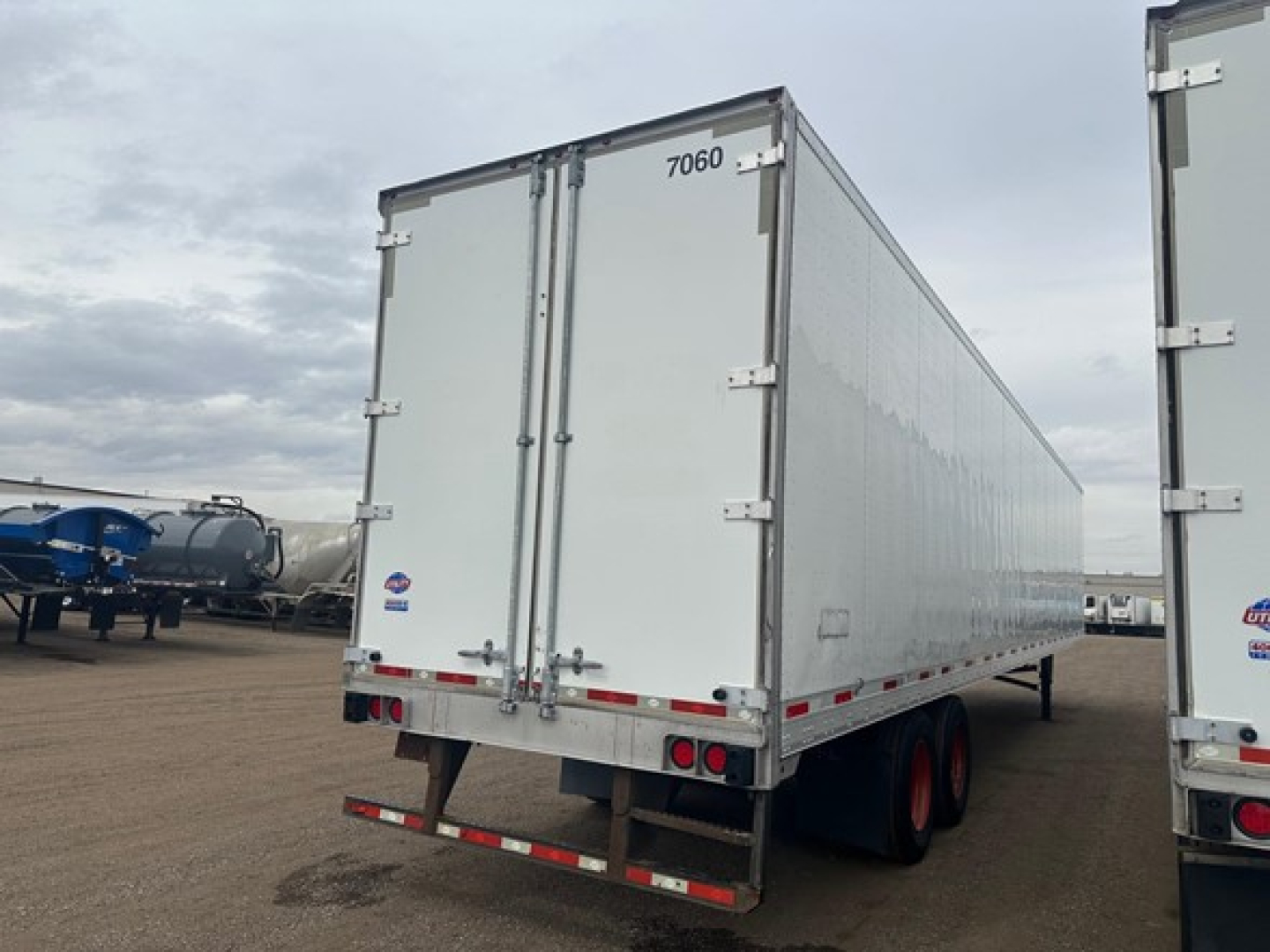 Utility 4000Dx trailer back view showing rear doors with '7060' number, dual rear lights, and white corrugated sides. Flatbed undercarriage visible with tandem axles and orange wheels.