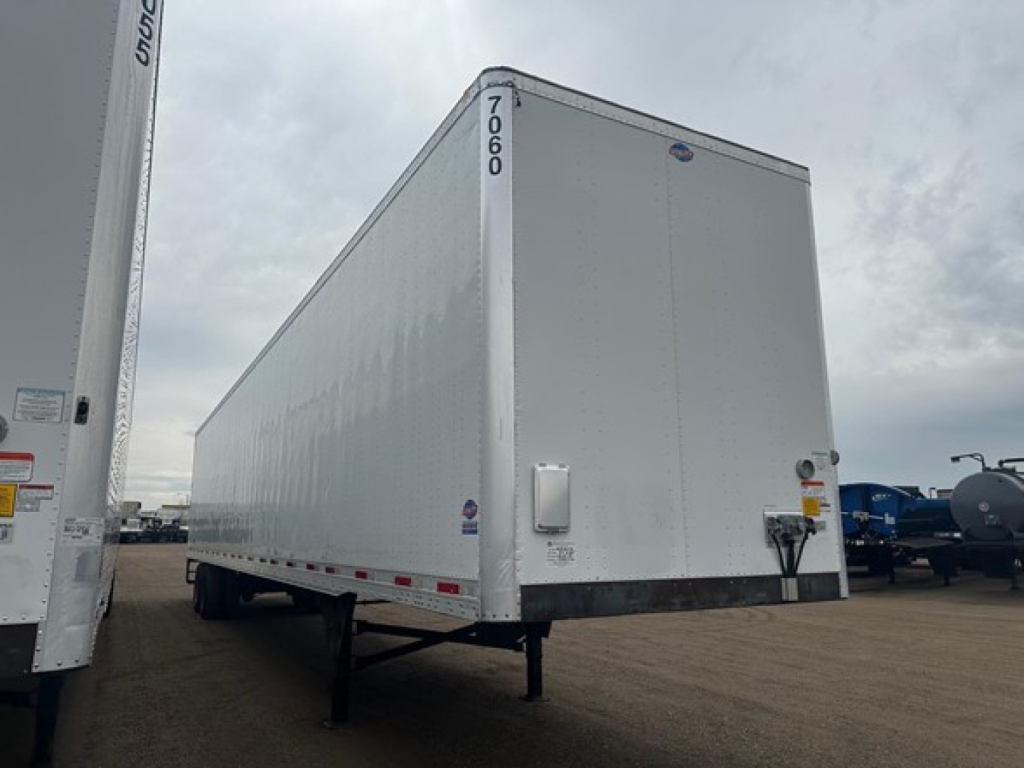 Utility 4000Dx trailer side view showing a white enclosed trailer with front cab and rear roller door, mounted on dual rear axles in a truck yard.