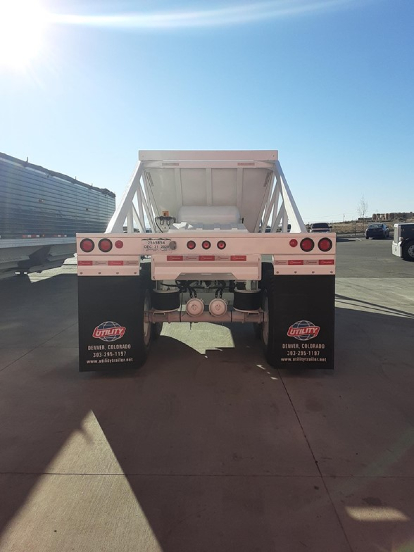 Dump trailer rear view showing wheel fenders, taillights, and hitch assembly with brand stickers on mudflaps.