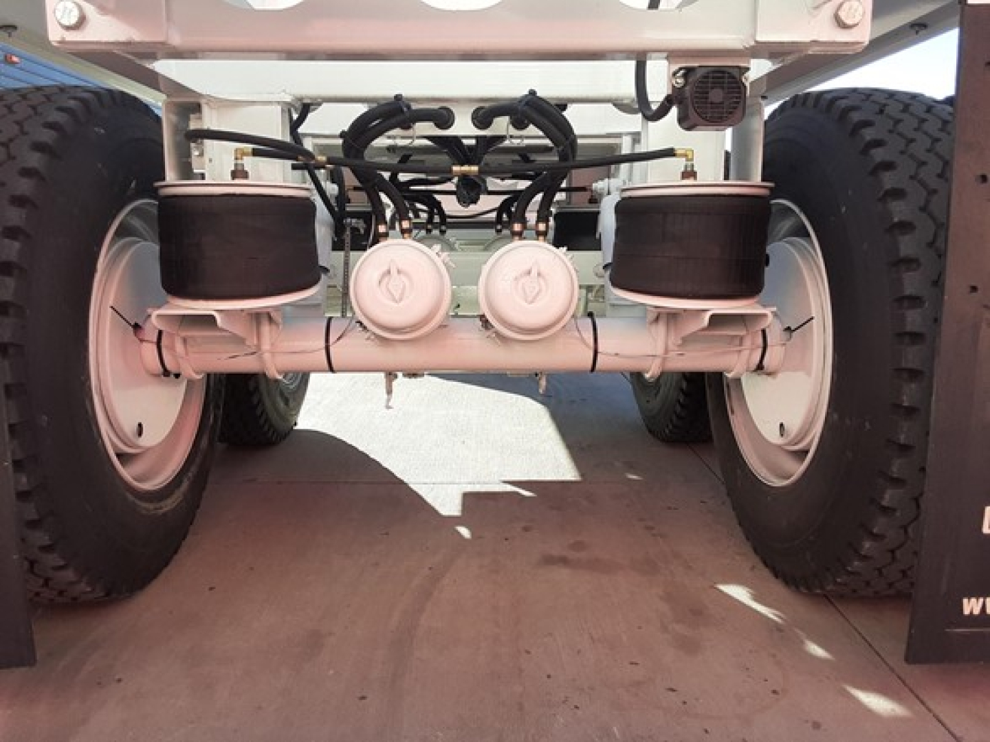 Ranco LW21-40 dump trailer rear view showing twin axles with dual round air filter housings and hydraulic lines; white frame and black tires.