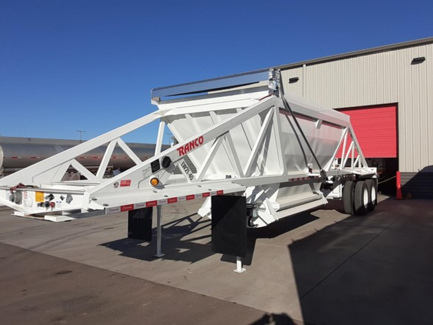 Ranco LW21-40 trailer in white, long extendable frame with triangular truss design, parked outdoors near a building with red door; trailer has dual rear axles and support legs.