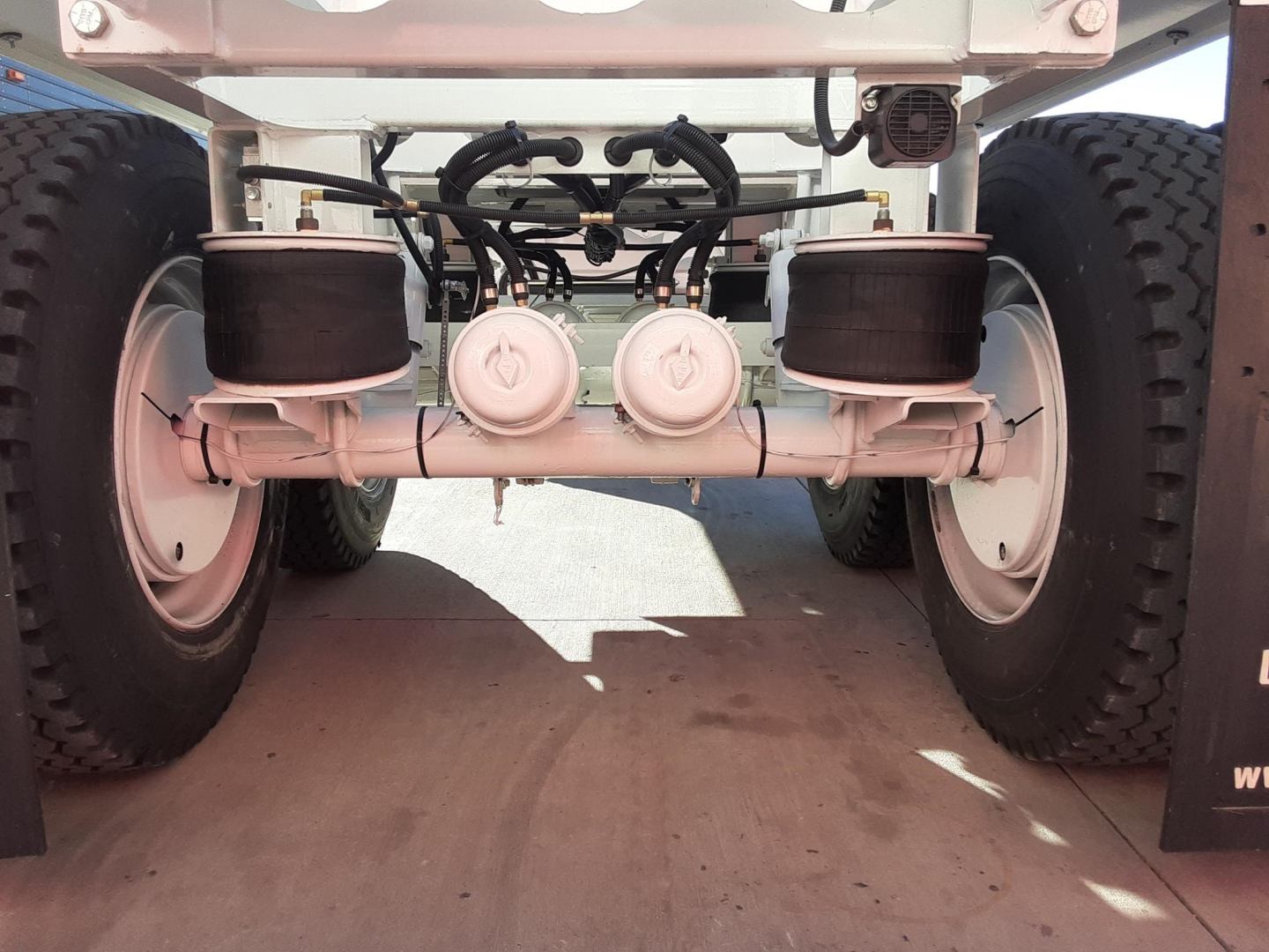 Ranco LW21-40 dump trailer undercarriage showing twin axles with dual air and hydraulic lines, center-mounted components, and large tires.