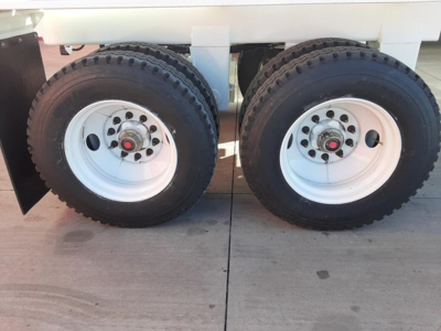 Dual rear wheels of a dump trailer showing white steel rims and black tires with red center hubs.