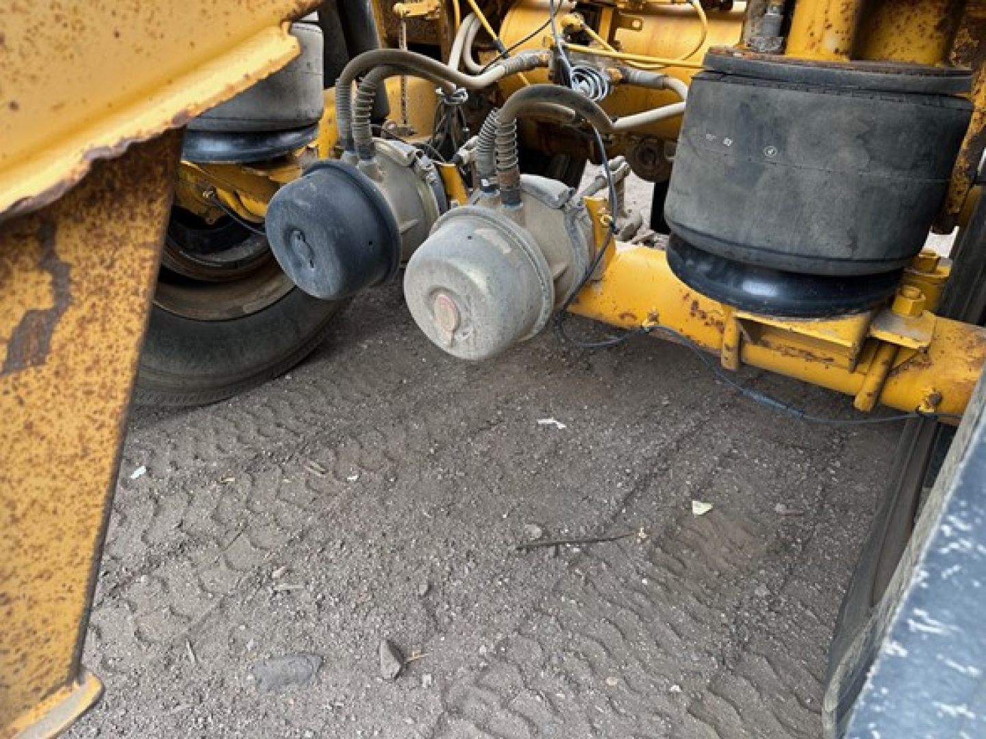 Trailer component area showing hydraulic lines and air tanks under a yellow Trail King air ride bottom dump trailer.