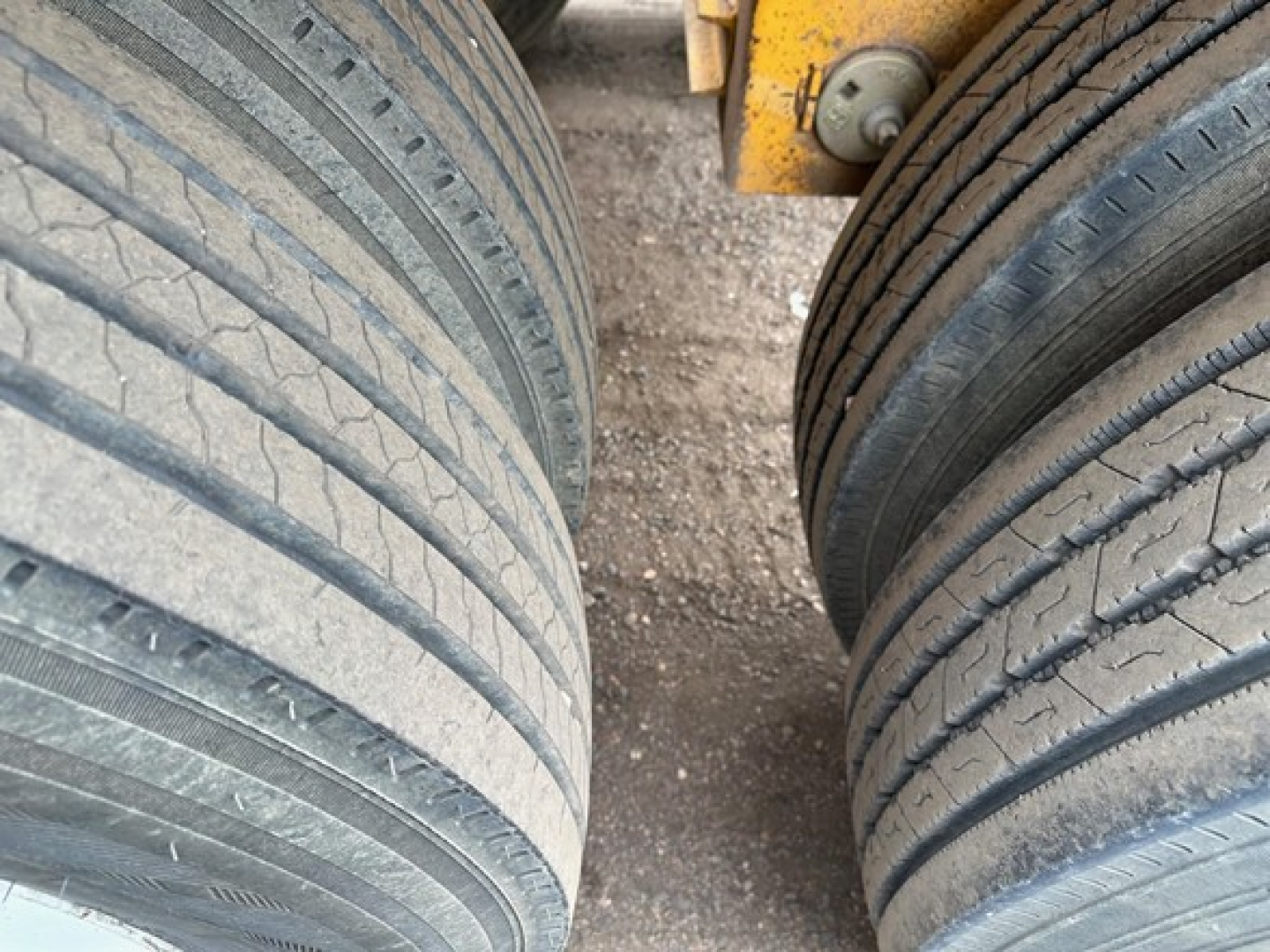 Trailer tires and undercarriage of a dump trailer showing treaded tires and part of yellow frame.