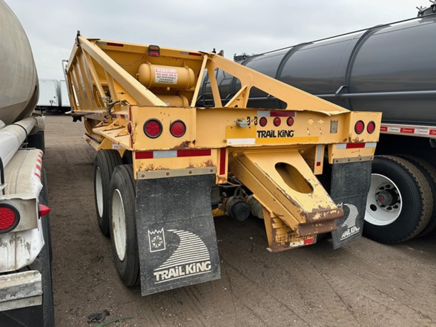 Trail King air ride bottom dump trailer viewed from rear-left with yellow paint, dual rear axles, mud flaps branded Trail King, and hydraulic dumping mechanism visible.