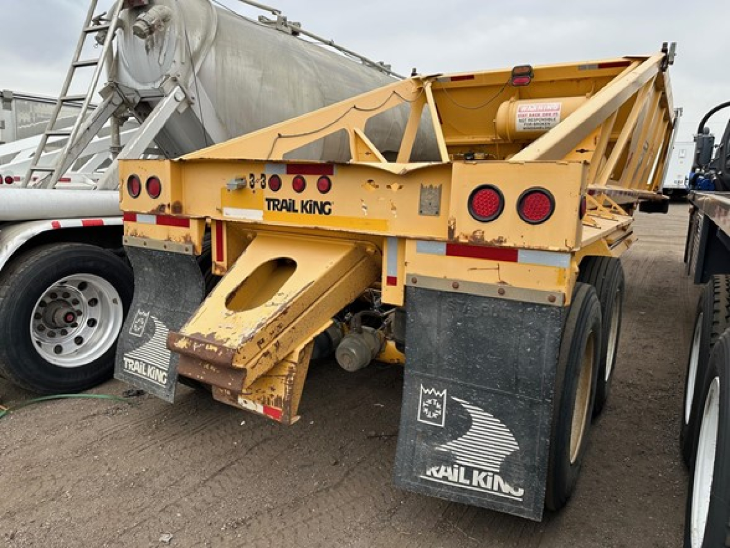 Trail King air ride bottom dump trailer showing rear view, yellow paint, twin axles, mud flaps with Trail King logos, and rear lights.