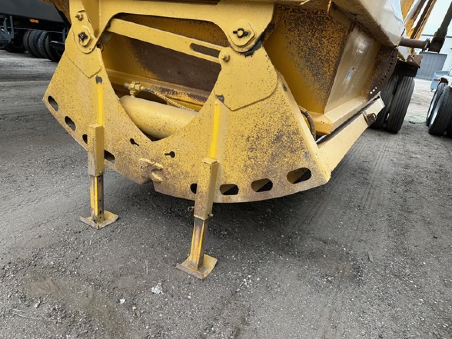 Bottom dump trailer from Trail King showing stabilizer legs and yellow steel frame with rust-like dust and ground grime.