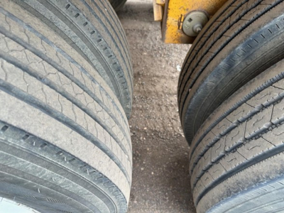 Trailer tires and undercarriage of a dump trailer showing treaded tires and part of yellow frame.