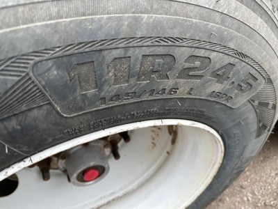 Trailer wheel close-up showing tire size 11R24.5 and white wheel with red hub cap cap.