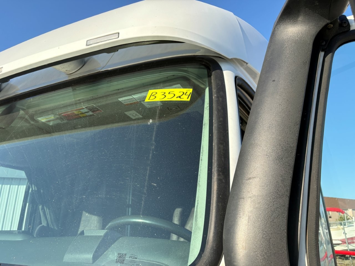 Truck cab window/front windshield with yellow stock tag reading B3524 in the upper corner and part of the Volvo VNL cab visible.