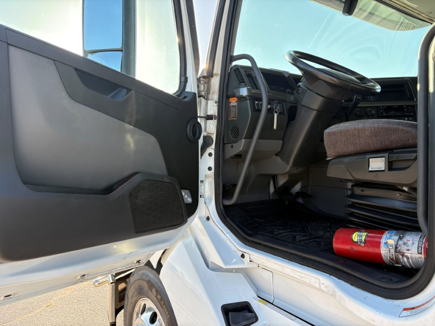 Volvo VNL64T860 truck cab interior shown from open driver door, steering wheel, dashboard, and seating; extinguisher mounted near floor; white exterior and step leading into cab.