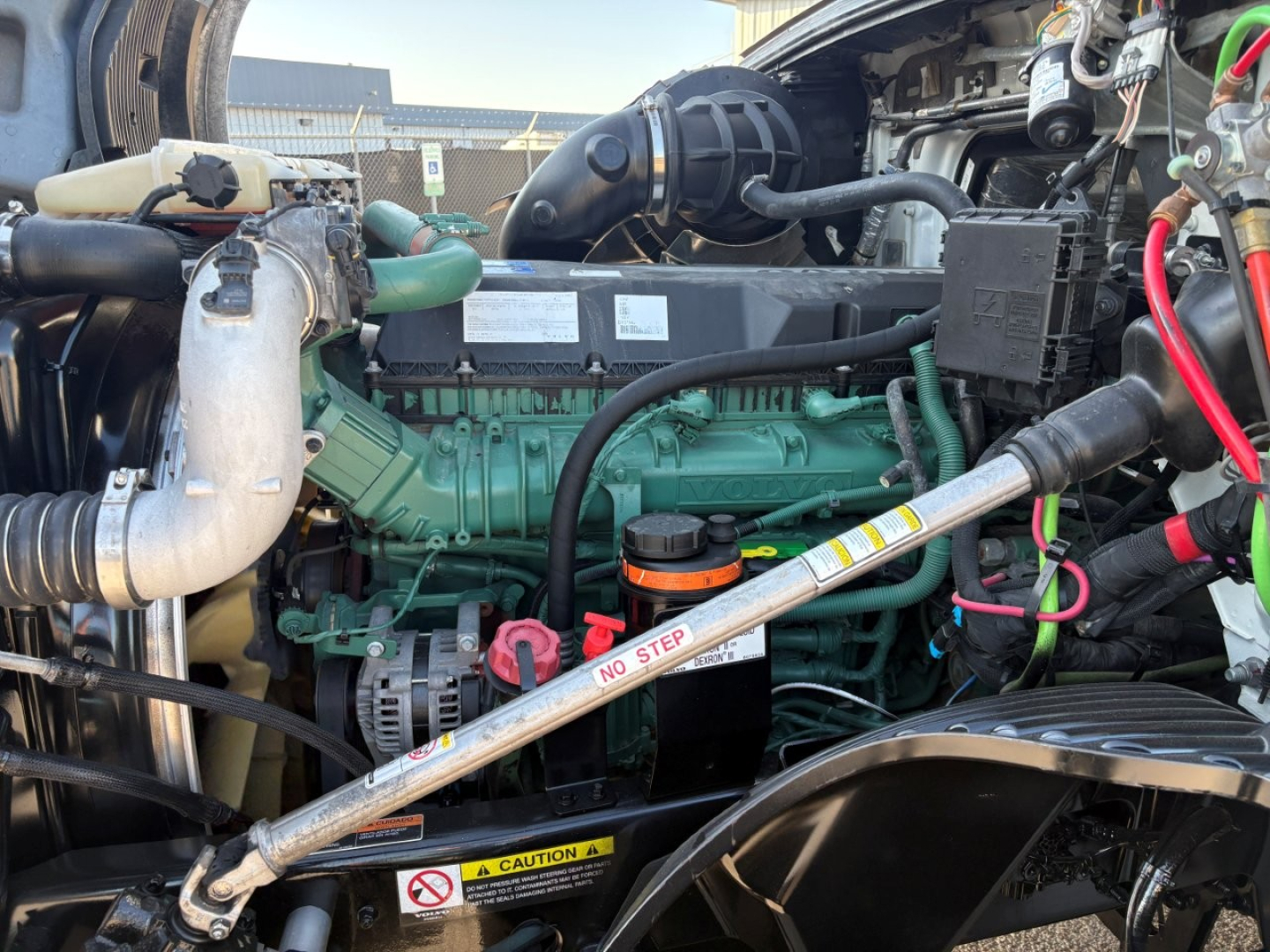 Volvo engine bay with a green engine, hoses, and a silver diagonal strut labeled NO STEP; surrounding components include a radiator, hoses, and black plastic manifolds.