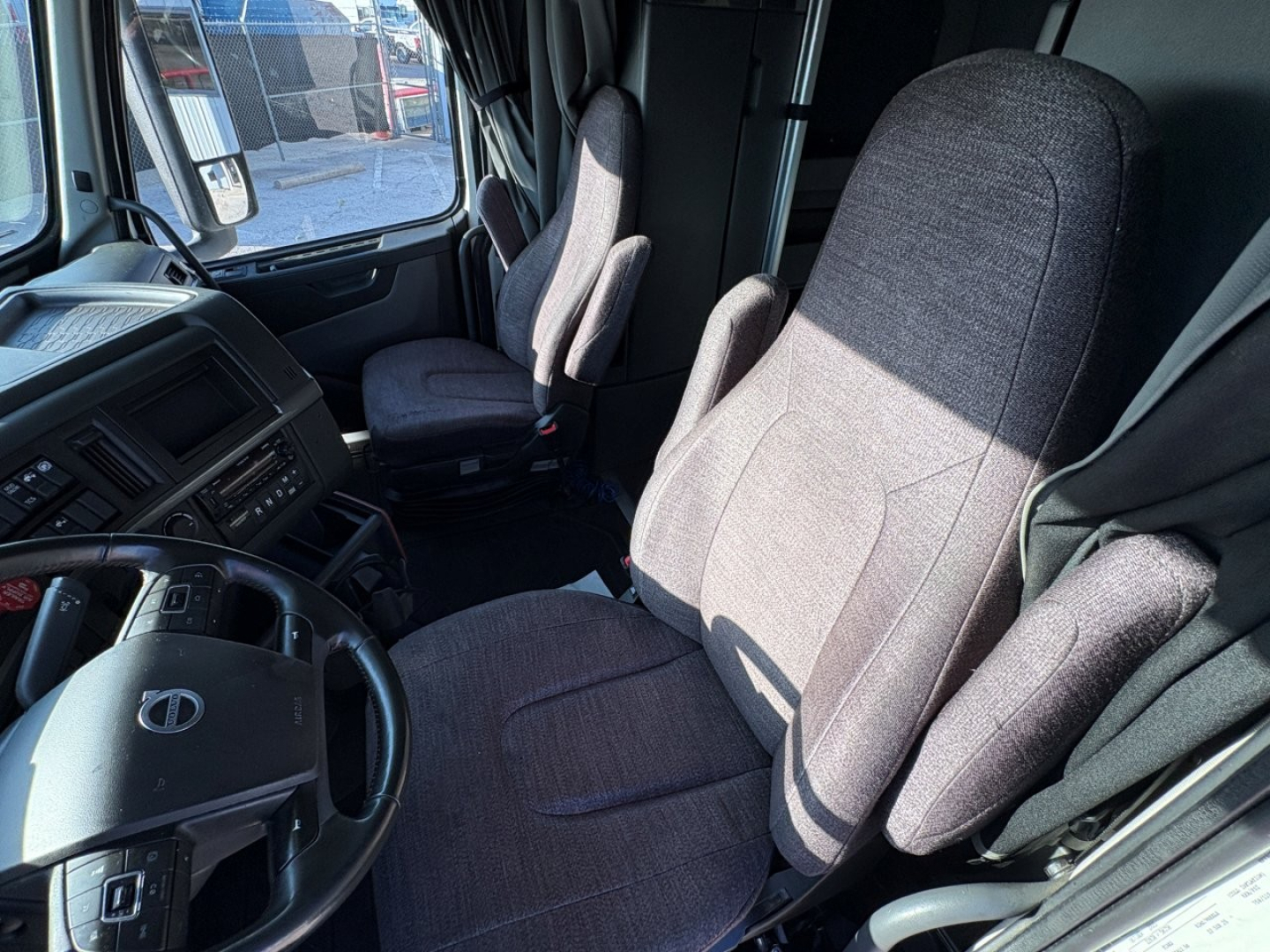 Volvo truck cab interior showing driver's seat and passenger seat with steering wheel and dashboard visible.