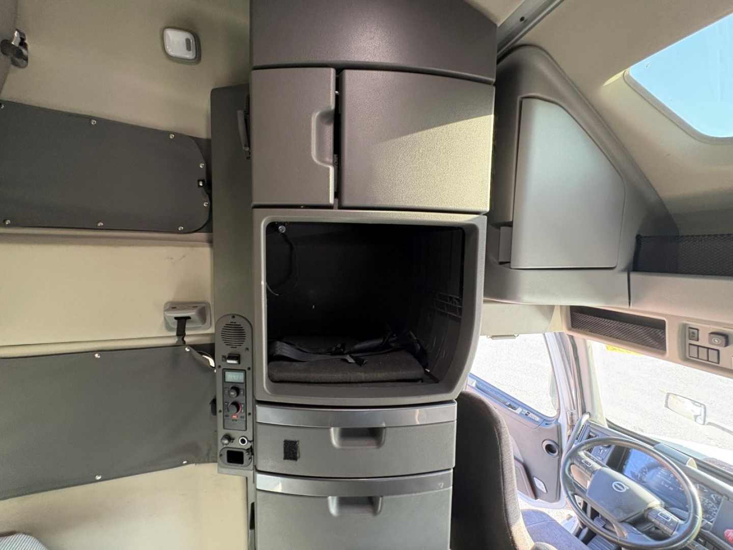 Cab interior of a Volvo VNL truck showing overhead storage bin and dash area, with a center console opening and control panel visible.