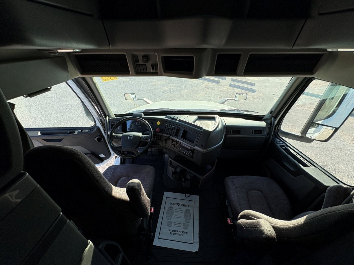 Volvo VNL interior cockpit view from driver seat showing steering wheel, dashboard, and two front seats; center console and overhead storage; windshield and side windows visible.