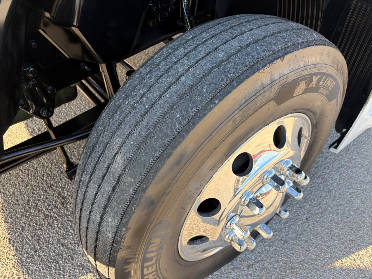 Volvo VNL64T860 truck wheel and tire close-up showing X Line tire and steel dual rear axle hub with lug nuts; front wheel visible with rim and hub may show suspension components.