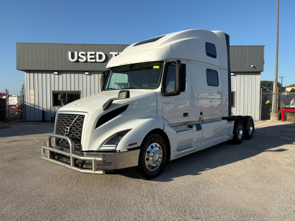 Volvo VNL64T860 semi truck in front of a used trucks lot showing cab with hood scoop and chrome bumper.