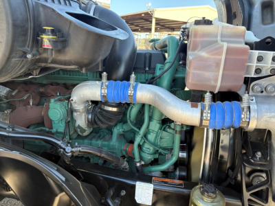 Volvo engine bay of 2024 VNL64T860 showing turbo inlet hose with blue couplers connected to green engine block and coolant reservoir.