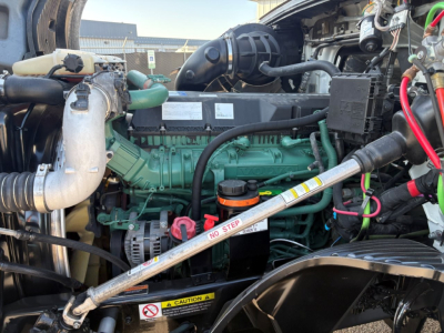 Volvo engine bay with a green engine, hoses, and a silver diagonal strut labeled NO STEP; surrounding components include a radiator, hoses, and black plastic manifolds.