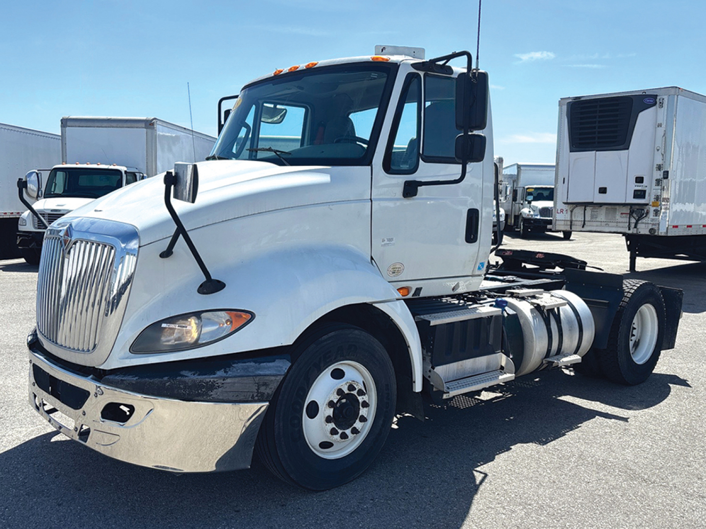 Truck cab showing International ProStar-style front with large chrome grille, white exterior, single sleeper cab, fuel tanks and rear wheels visible.