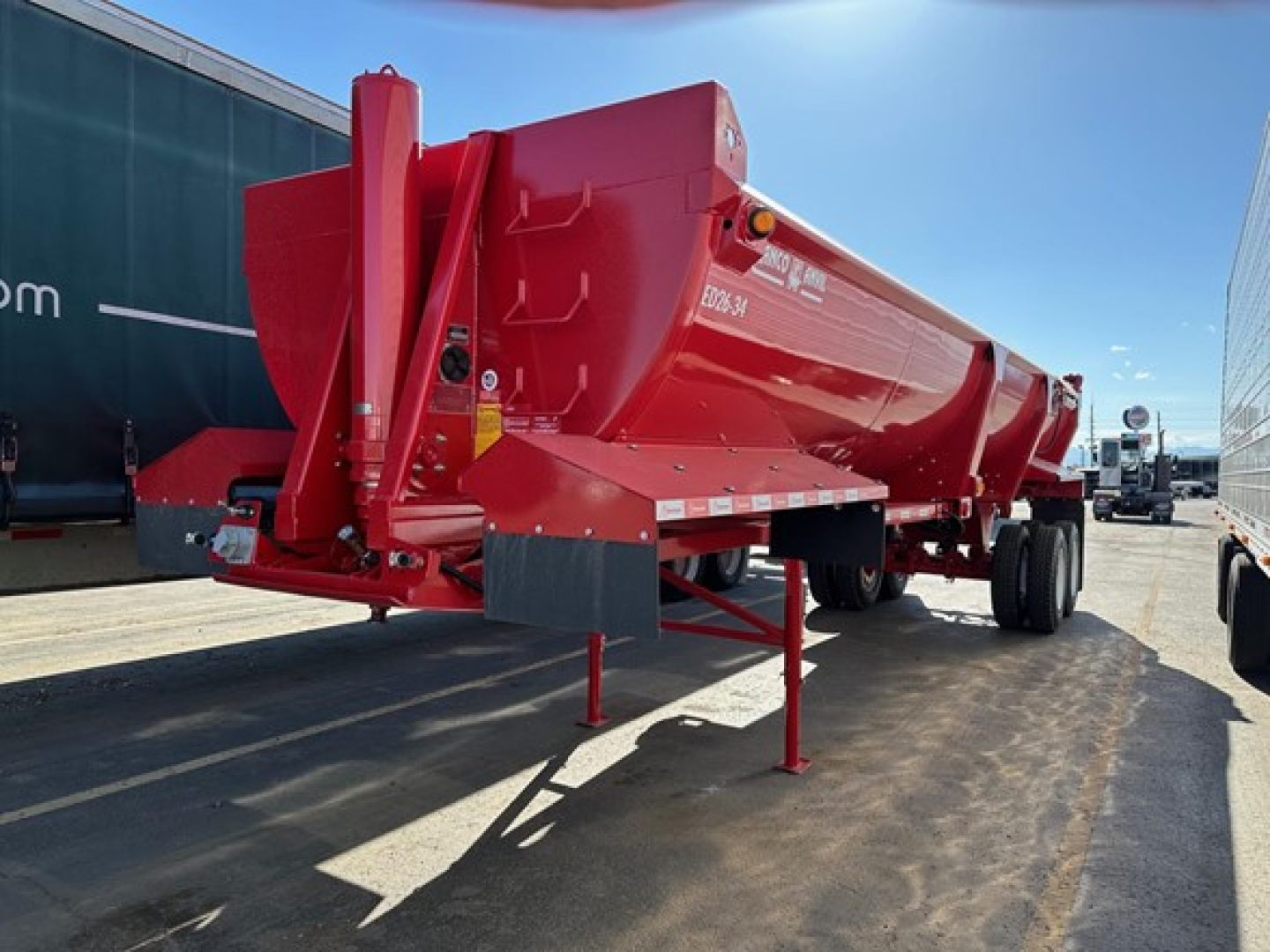 Dump trailer in red showing ED26-34 model label and support legs, with chassis and wheels visible.