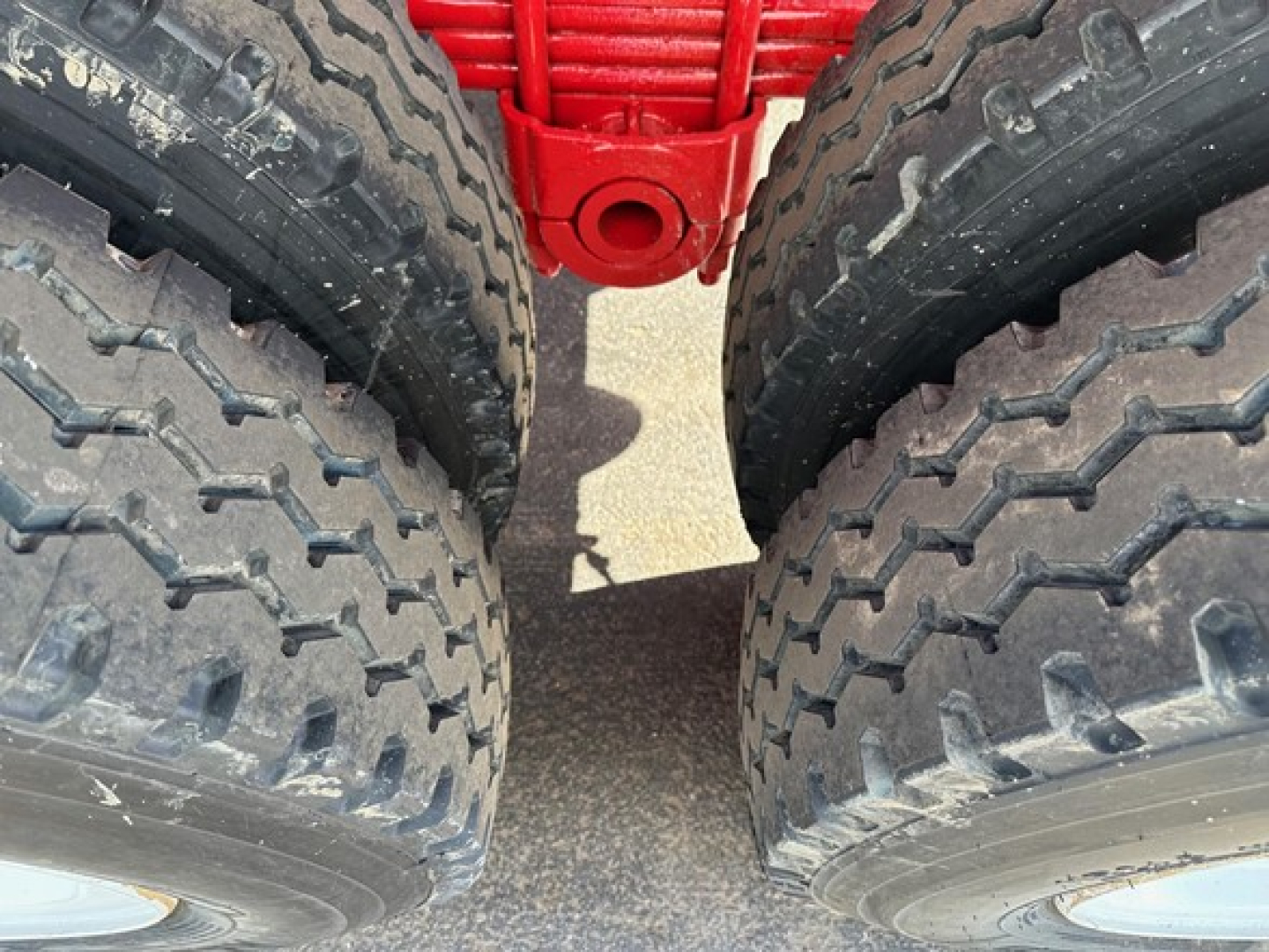 Two large truck tires on a red trailer chassis with treads visible, close-up view between wheels.