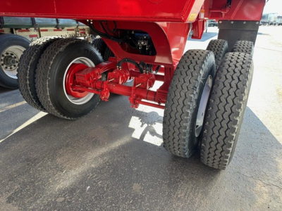 Ranco Ed26-34 dump trailer undercarriage with red suspension, dual rear axles and heavy-duty tires. Visible: red painted frame and hubs, components, and wheel assembly.