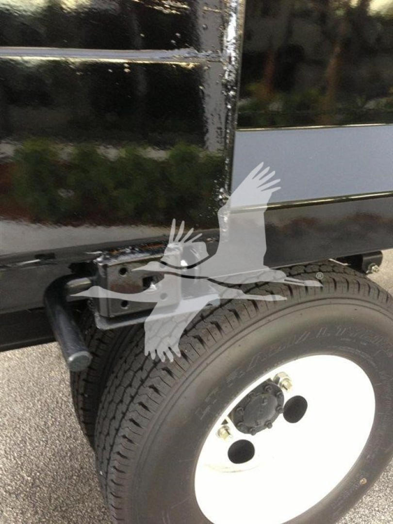 Truck bed side showing rear wheel and undercarriage components near the dump bed; includes black metal frame and white steel wheel with tire.