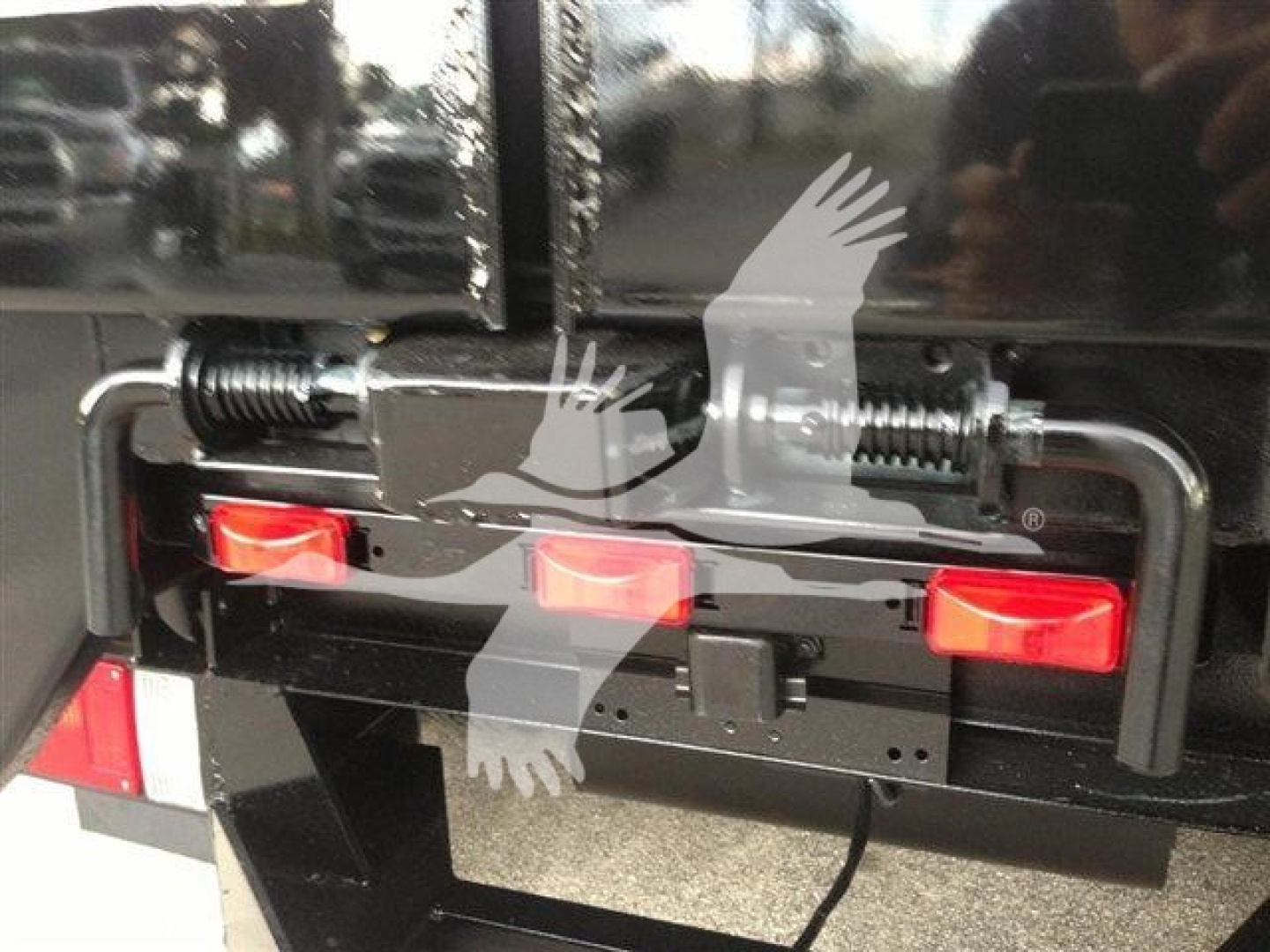 Truck tailgate area showing hydraulic latching mechanism on a dump truck with red reflectors and black metal frame.