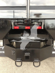 Dump truck rear showing hitch and bumper with two red taillights and lift mechanism.