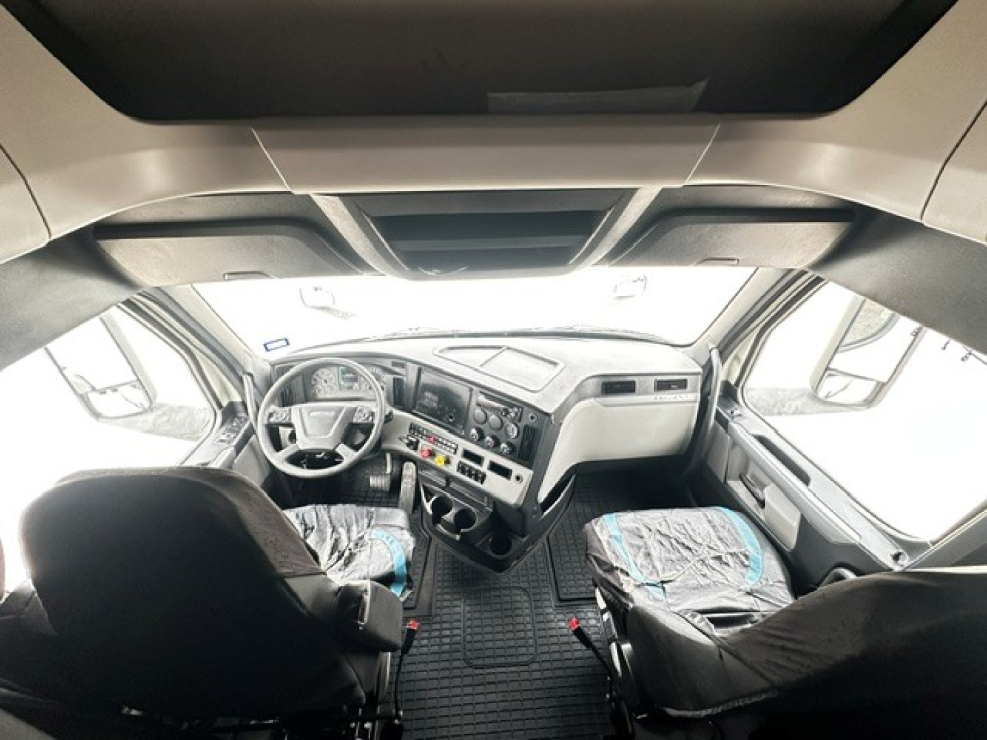 Cab interior of a Freightliner Cascadia 126 truck showing steering wheel, dashboard, and two front seats with protective covers.