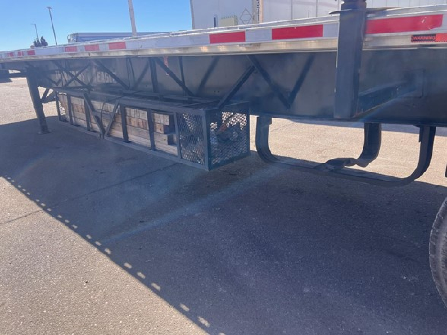 Transit truck trailer undercarriage and support structures on a Transcraft spread air combo flatbed showing side rails and underdeck storage cage.