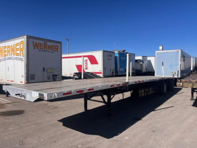 Transcraft spread air combo flatbed trailer in a truck yard with other trailers in background; flatbed deck visible with landing gear and mobile trailers.